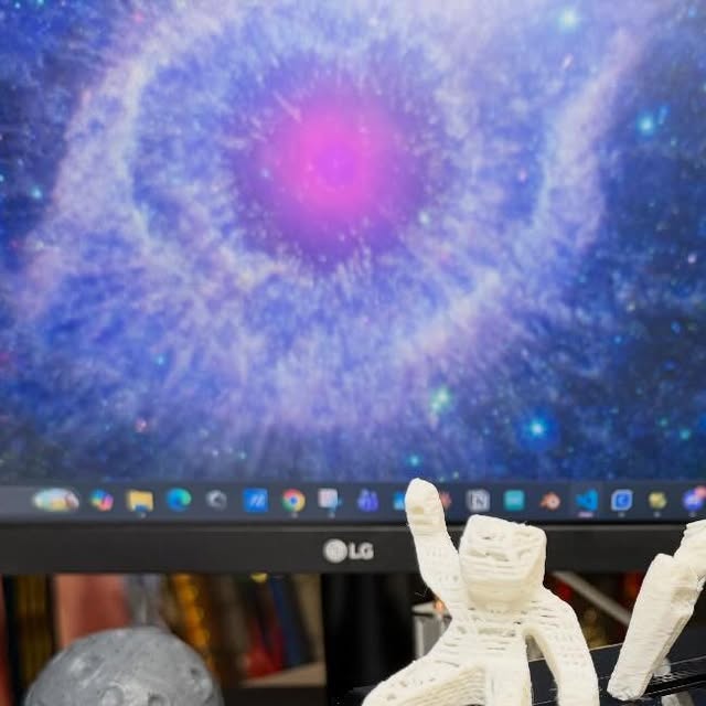 A white 3D-printed figure on Aran’s desk, with a space image on the monitor behind it